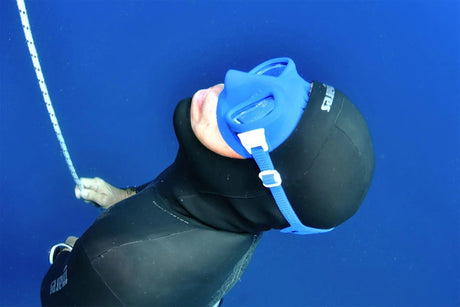 Freediver wearing a low-volume mask descending along a dive line in clear blue water