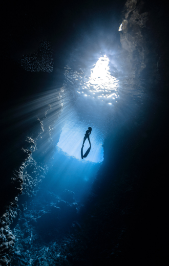 Person freediving in a cave with sunlight filtering through.